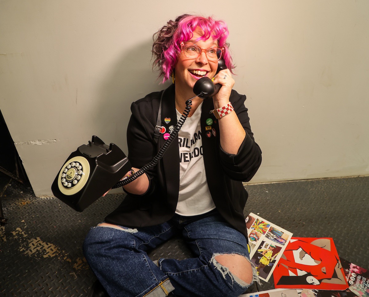Robyn Sayles sitting on the floor laughing into a black rotary phone, surrounded by comic books